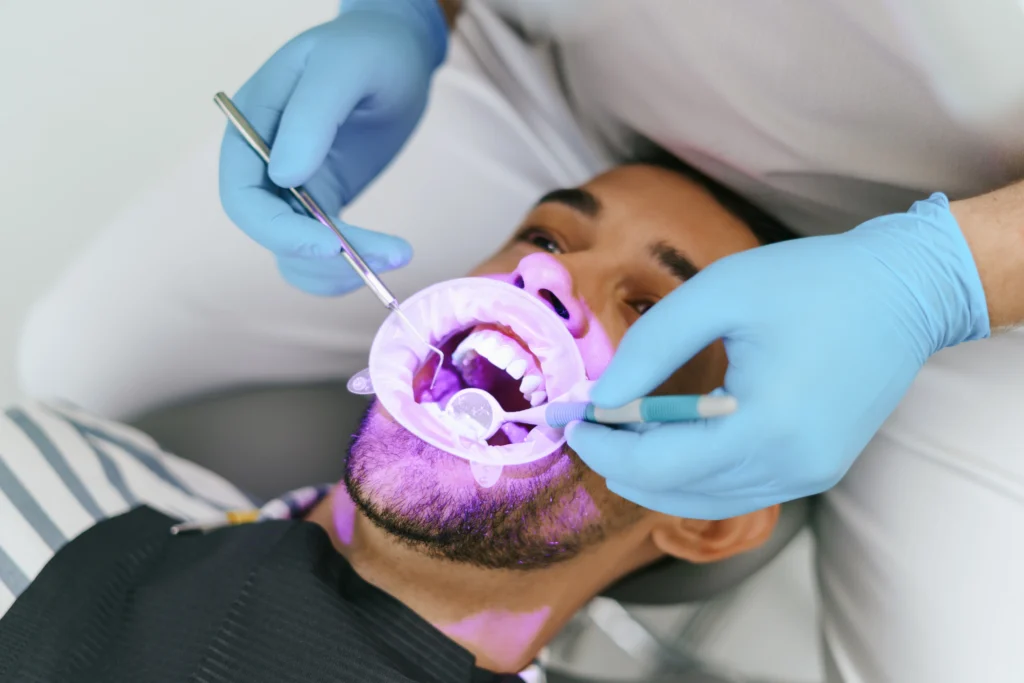 Patient undergoing professional teeth whitening with LED light and dental tools.