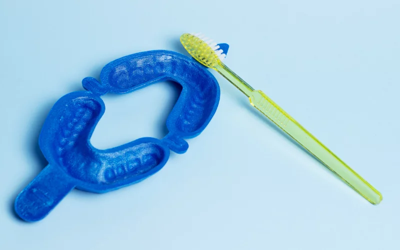 Blue dental mouthguard and yellow toothbrush on light blue background