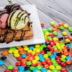 Waffles with ice cream and colorful candies on wooden table