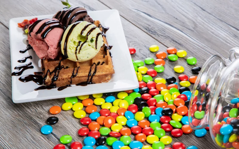Waffles with ice cream and colorful candies on wooden table