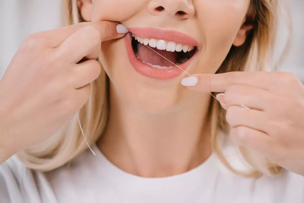 Woman practicing dental hygiene by flossing teeth.