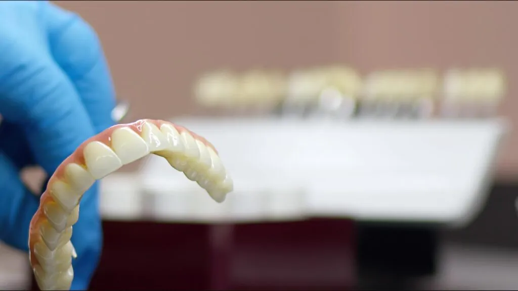 Close-up of zirconia dental bridge held by dentist in a gloved hand.